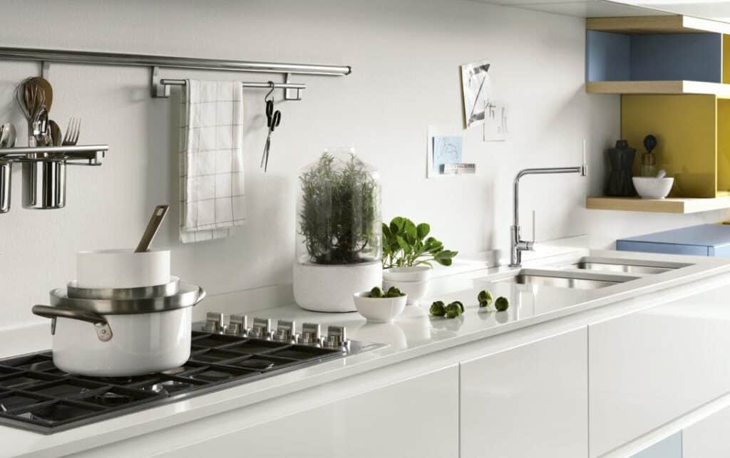 Modern kitchen with a gas stovetop, white cookware, herbs in a pot, and decorative shelving.