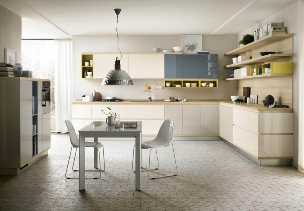Modern kitchen with beige and blue cabinets, white dining table with two chairs, geometric patterned floor, and pendant light.