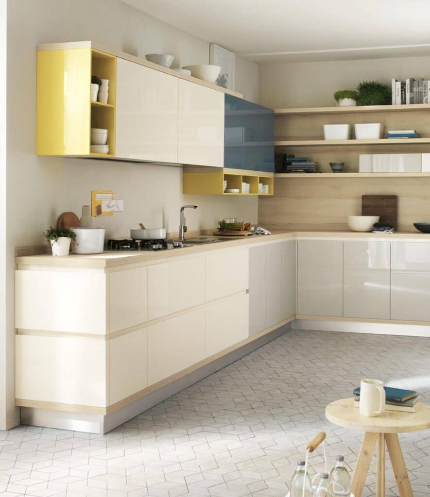 Modern kitchen with glossy cabinets in beige, yellow, and blue, wooden countertops, open shelving with dishes and plants, and a geometric-patterned tile floor.