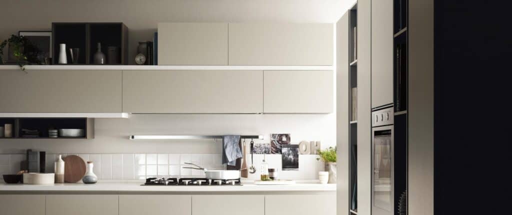Modern kitchen with minimalist cabinetry, wall-mounted oven, stove, and various kitchen items on the countertop.