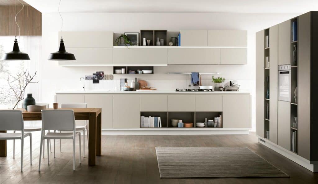 Modern kitchen interior with beige cabinets, wooden dining table with white chairs, and hanging black pendant lights.