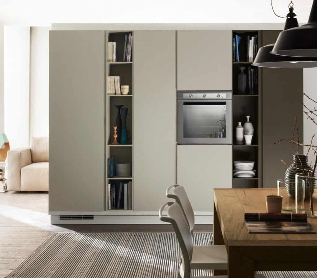 Modern kitchen with built-in oven, open shelves with books and decor, wooden dining table, and chairs.
