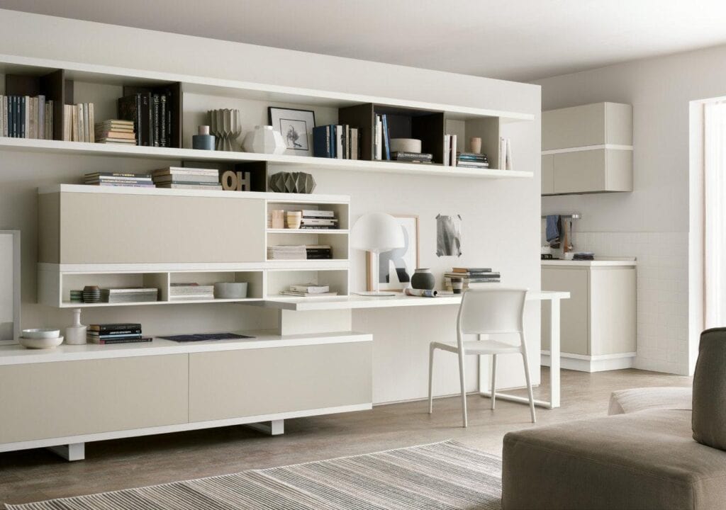 Modern living space with a minimalist design featuring wall-mounted shelves filled with books and decorative items, a sleek desk with a lamp, and a chair.