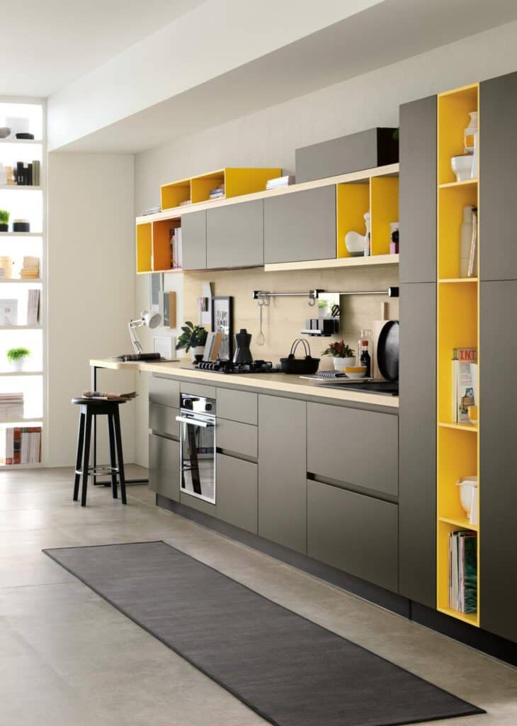 Modern kitchen with gray cabinets and yellow accents, featuring open shelving, a countertop with a stove, and a long black floor mat.