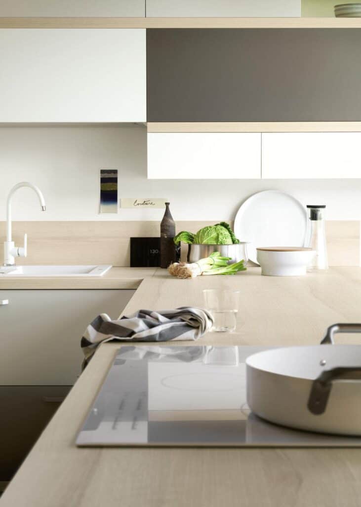 Modern kitchen interior with beige cabinetry, white sink and faucet, vegetables on the countertop, and cooking items.