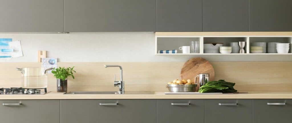 Modern kitchen counter with stainless steel pot, fresh herbs, and vegetables.