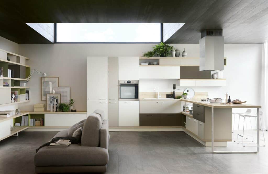 Modern open-plan kitchen and living area with sleek cabinetry, a built-in oven, an island with bar stools, and a gray sofa.