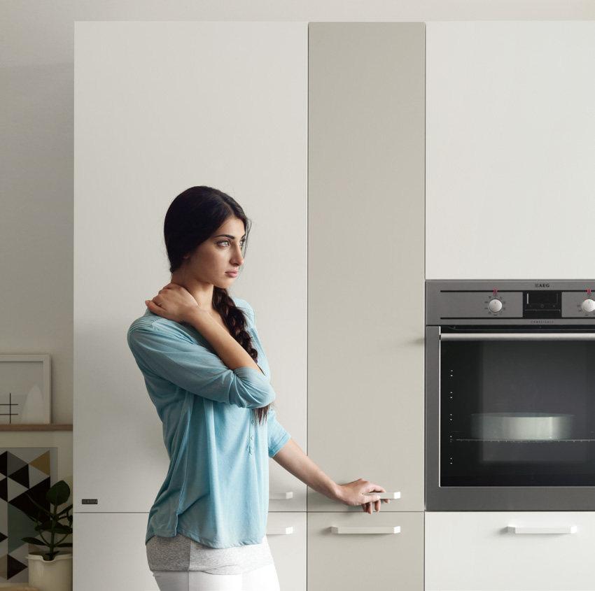 Woman in a light blue shirt standing in a modern kitchen next to a built-in oven.