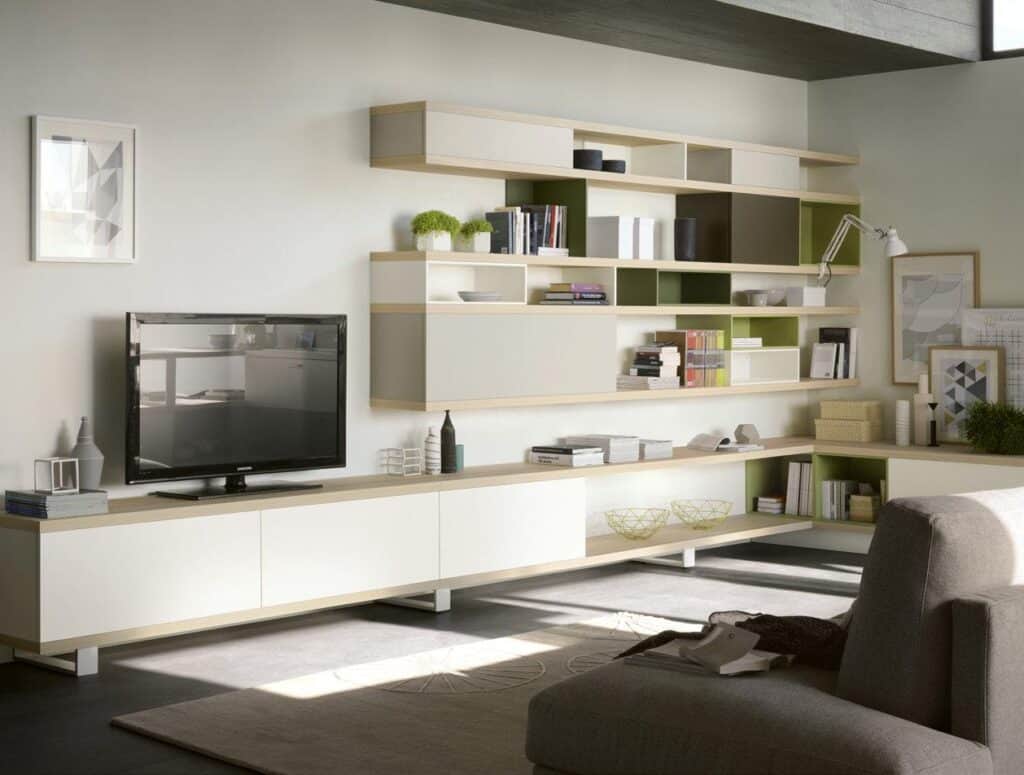 Modern living room with modular wall shelving and cabinets, a flat-screen TV on a low cabinet, books and decorative items on shelves, a gray armchair, and a minimalistic color scheme.