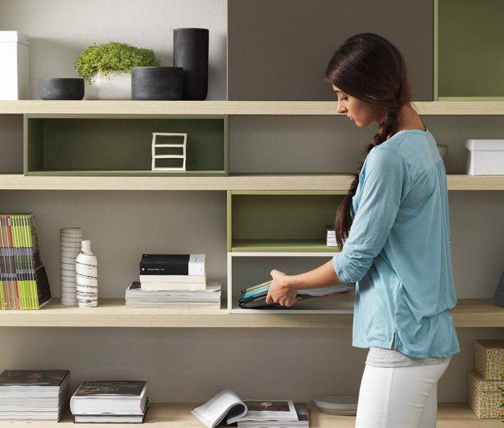 A woman organizing items on a modern wooden bookshelf with a mix of books, magazines, and decorative objects.