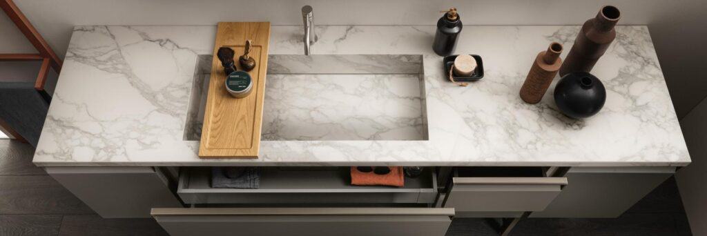 Marble bathroom countertop with a sink, wooden board, soap dispenser, and decorative vases.