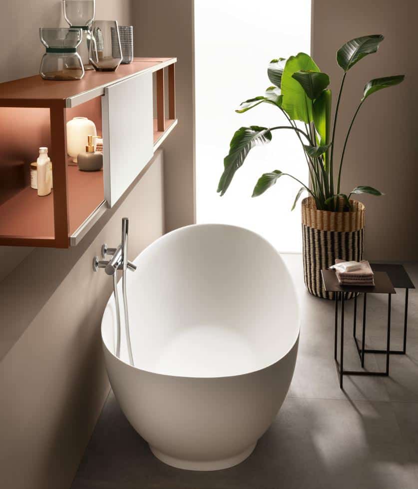 Modern bathroom with a white freestanding tub, a wooden shelf with decor items, and a large potted plant.