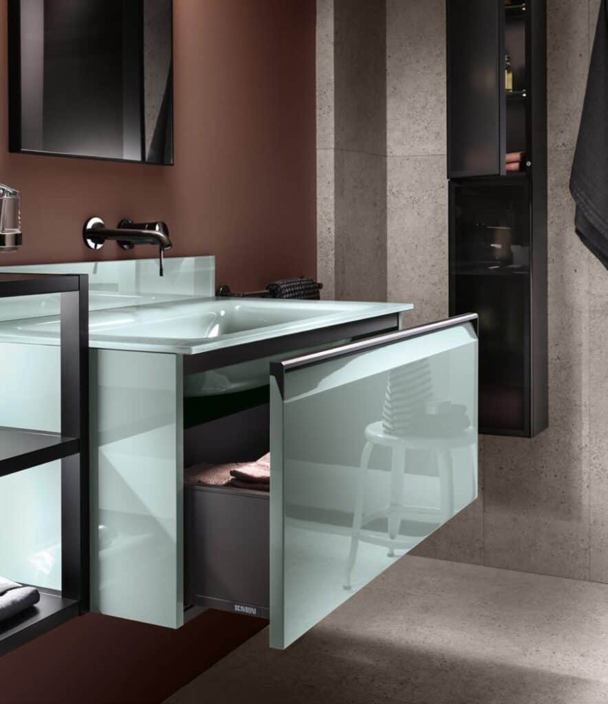 Modern bathroom with a glass-front vanity drawer open, revealing towels inside.