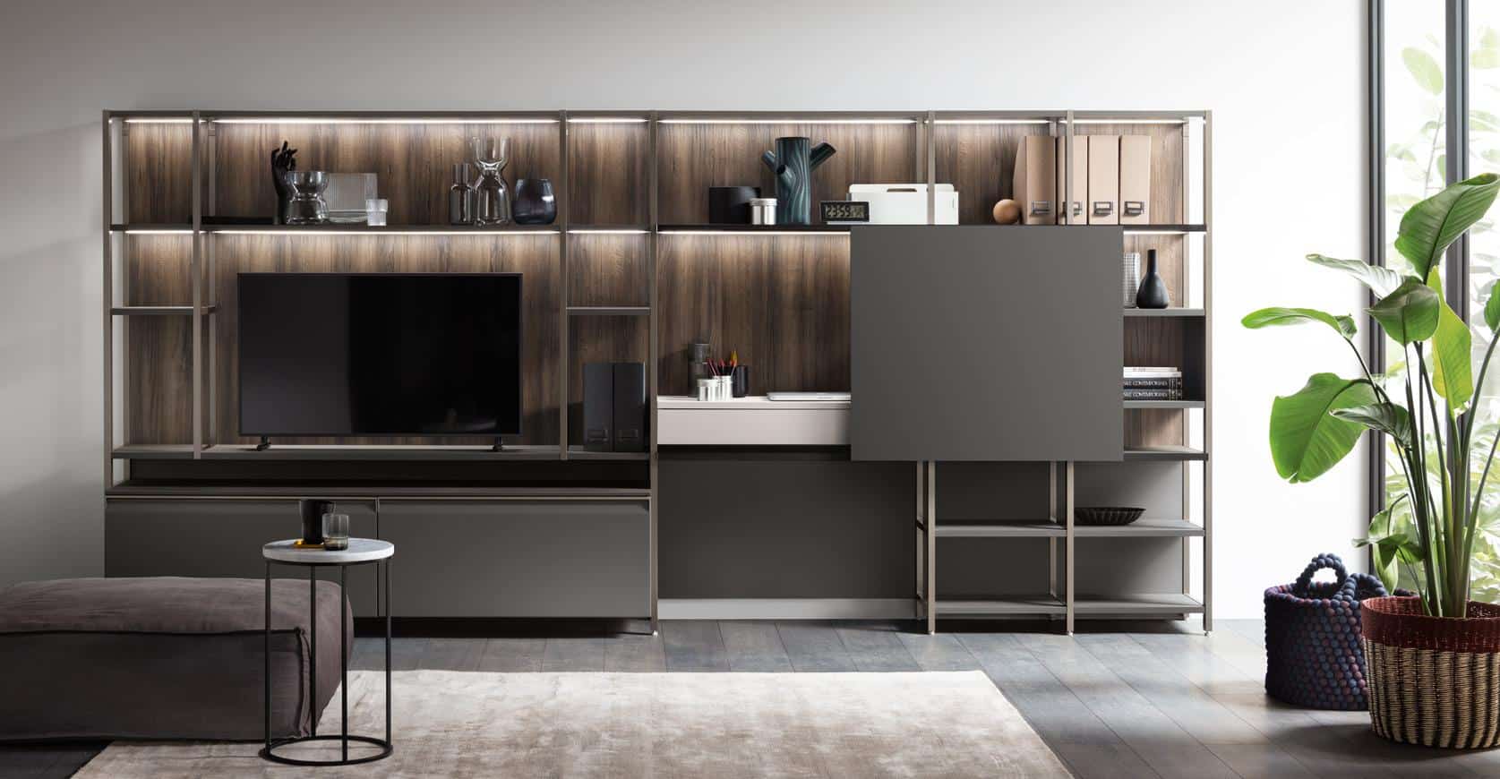 "Modern living room interior with a wall-mounted entertainment center featuring a TV, shelves with decorative items, and storage cabinets, alongside a plant and a basket near a large window."
