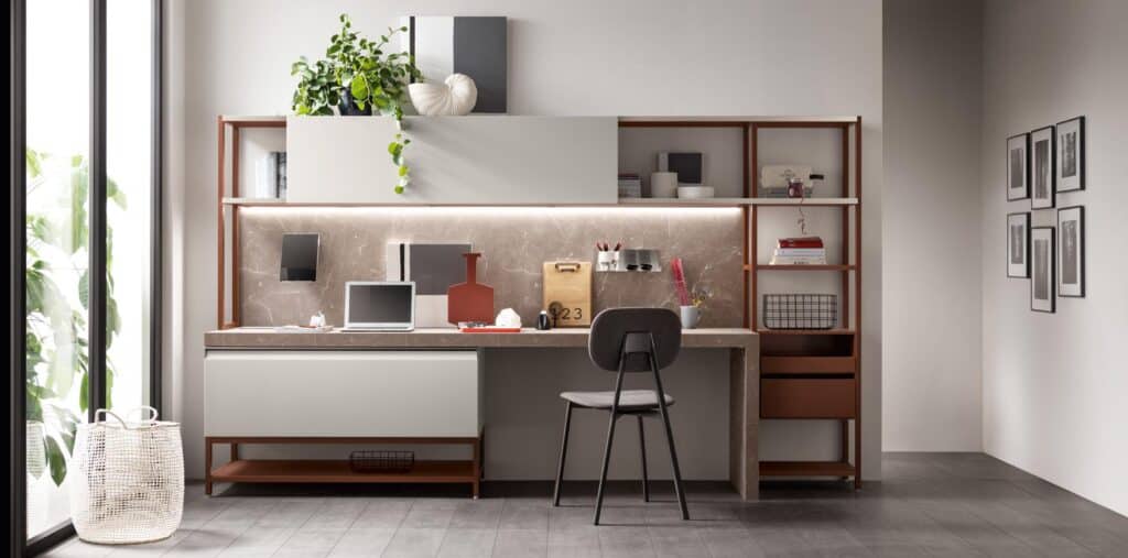 Modern home office setup with a desk, chair, and shelving, featuring a laptop, decorative items, and a potted plant, near a large window.