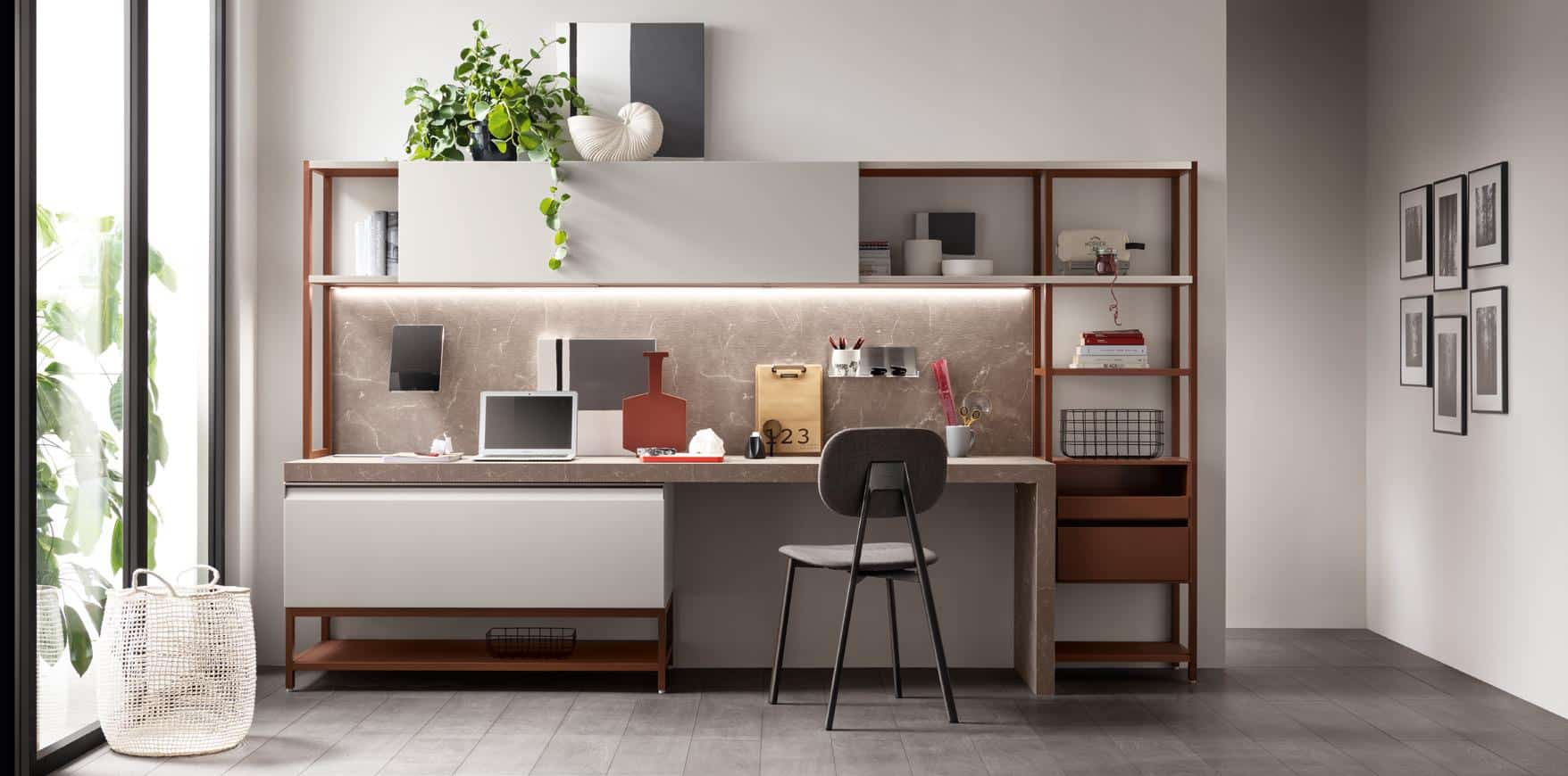 Modern home office setup with a desk, chair, and shelving, featuring a laptop, decorative items, and a potted plant, near a large window.