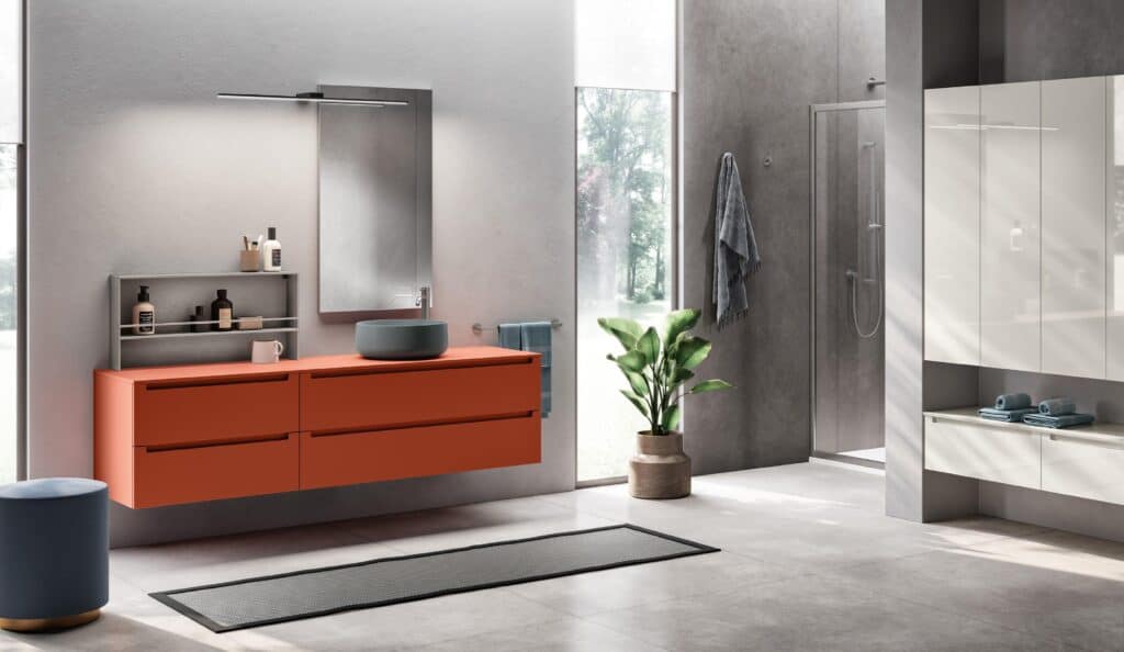 Modern bathroom with an orange vanity, gray sink, mirror, wall-mounted shelves, and a glass shower.