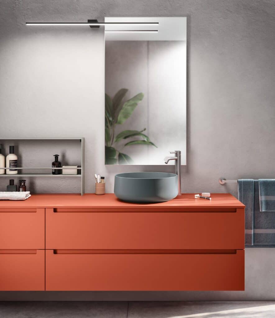 Modern bathroom with an orange vanity, round gray sink, mirror, and toiletries.