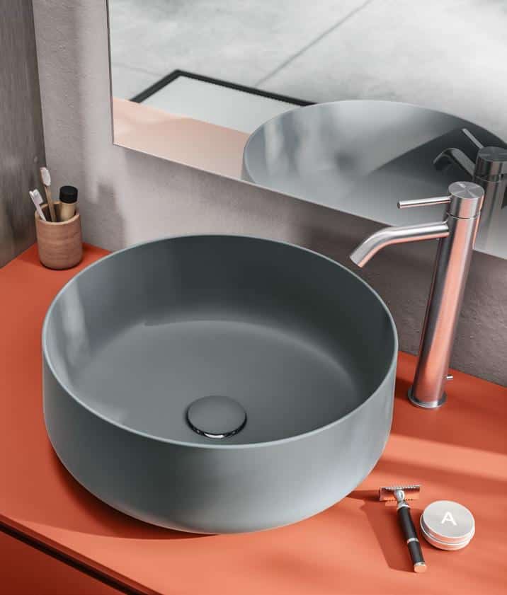 Modern bathroom sink on an orange countertop with a silver faucet and toiletries nearby.