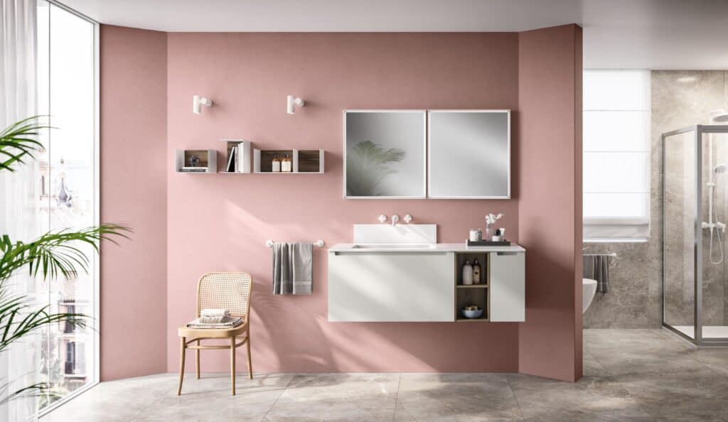 Modern bathroom with pink walls, a floating white vanity, wall-mounted shelves, a mirror, a rattan chair, large window, and a glass-enclosed shower.