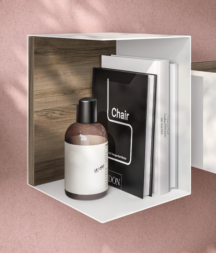 A modern wall shelf with a wooden back, holding a black &quot;Chair&quot; book, a white Le Labo bottle, and additional white books, against a pink wall.