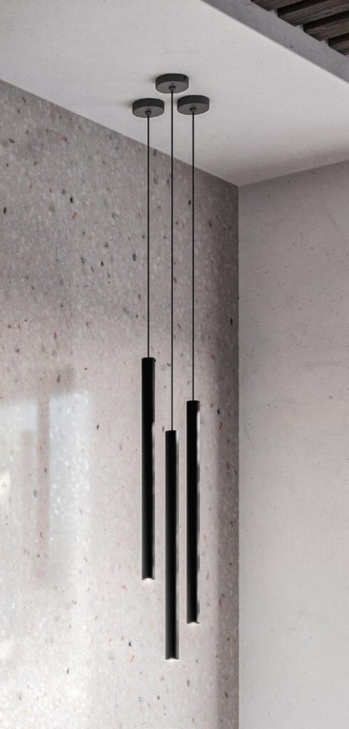Modern black pendant lights hanging from a ceiling with a speckled stone wall background.