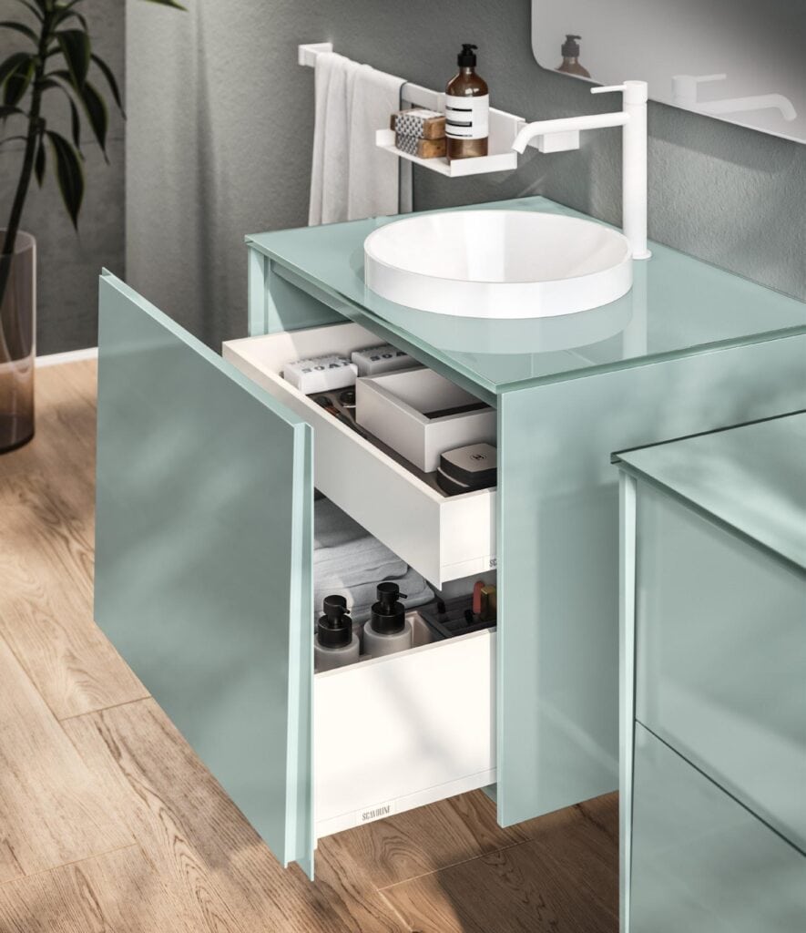 Modern bathroom vanity with a light green cabinet, open drawers, a round white sink, white faucet, and toiletries on a shelf.