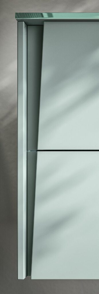 Close-up of a minimalist, light gray cabinet with an angled drawer front and a glass top.