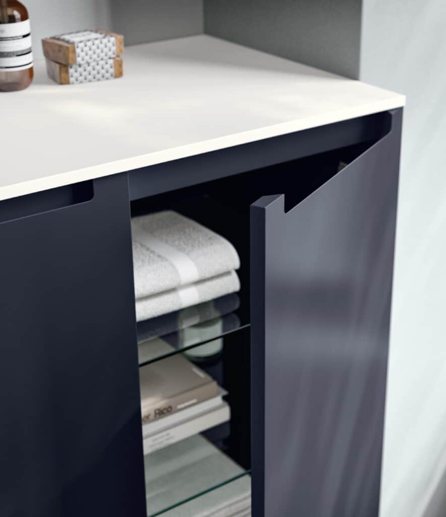 Open cabinet door with glass shelves inside, displaying folded towels and books.