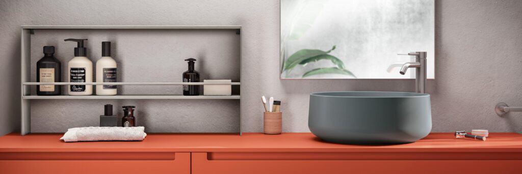 Modern bathroom interior with a gray bowl sink, faucet, and orange countertop; shelves with toiletries, mirror reflecting greenery, and grooming items.