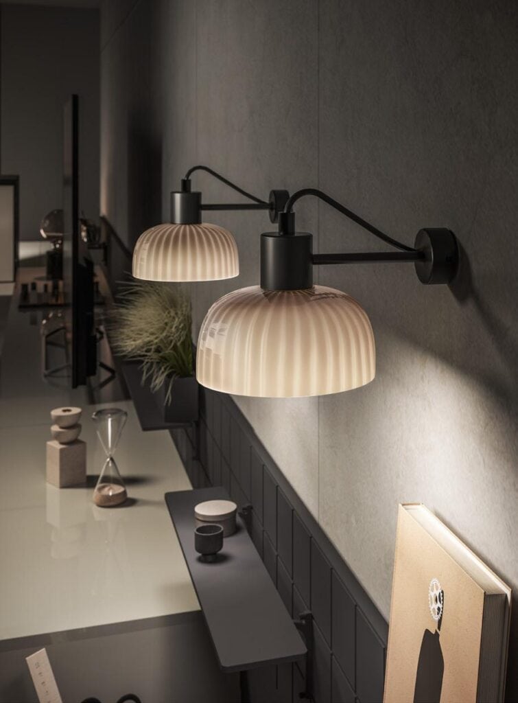 Two wall-mounted lamps with ribbed glass shades illuminating a modern interior space, featuring a shelf with decor items like an hourglass and minimalist objects.