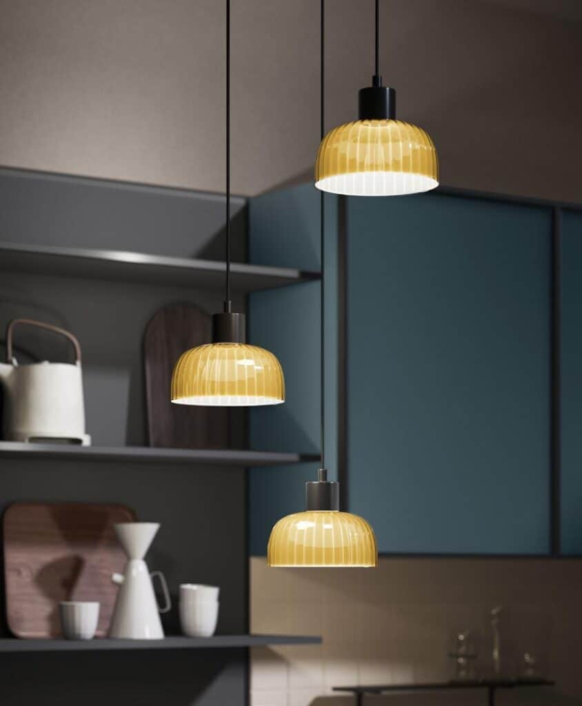 Three modern pendant lights with yellow ribbed glass shades hanging in a kitchen.