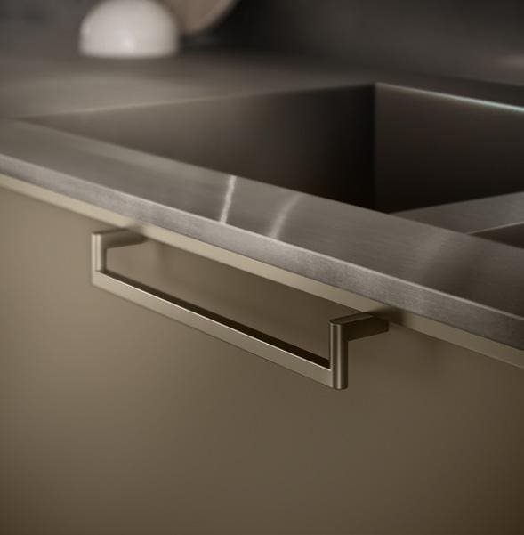 A close-up of a modern kitchen drawer with a metallic handle, beneath a stainless steel countertop.