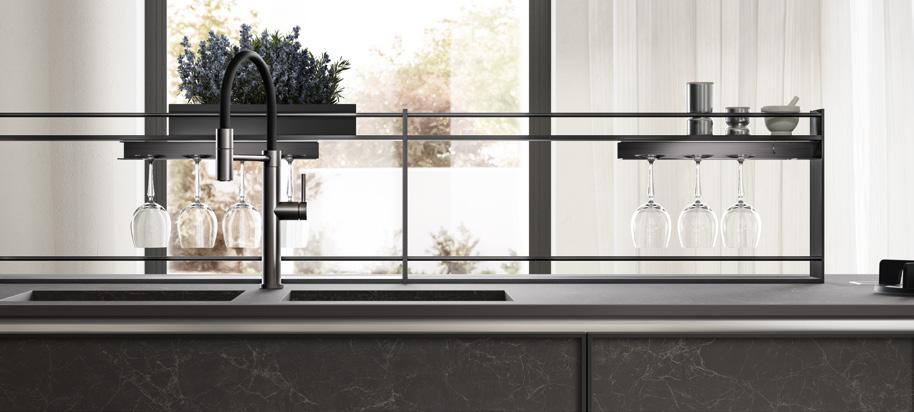 Modern kitchen counter with hanging wine glasses, black faucet, and decorative plants by a window.