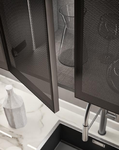 Kitchen detail with a sink, marble countertop, metal mesh cabinet doors, and a glass carafe inside the cabinet.