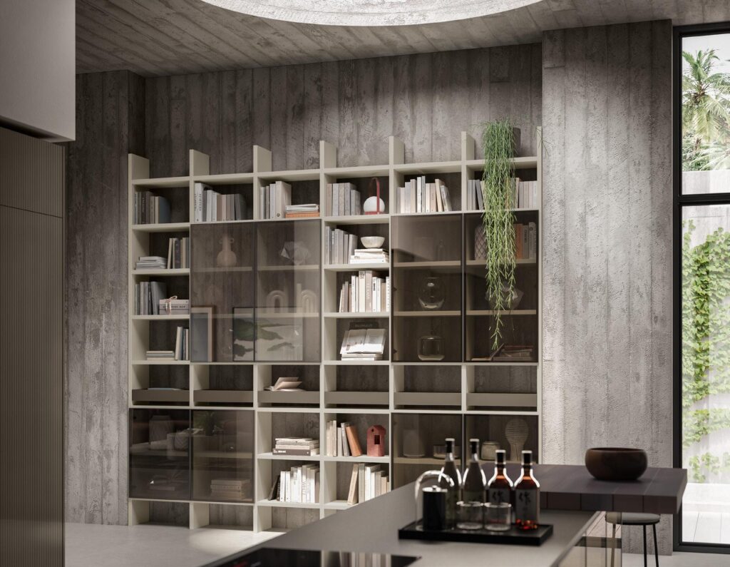 Modern interior with a large bookshelf against a concrete wall, containing books, decorative items, and a hanging plant; a kitchen counter with bottles and glassware in the foreground, and a window with a view of greenery.