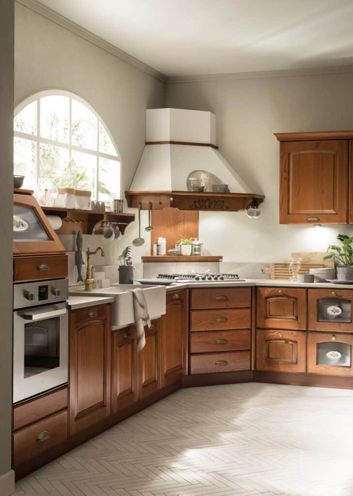 Traditional kitchen with wooden cabinets, white countertops, a farmhouse sink, and a gas stove under a decorative range hood. A large arched window provides natural light.