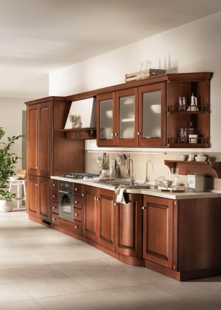 Traditional wooden kitchen cabinets with glass-panel doors, countertop, sink, oven, stove, and decorative shelves.