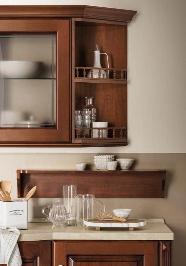 Kitchen with dark wood cabinets, shelves with glassware and ceramics, and a countertop with a kettle, glasses, and utensils.