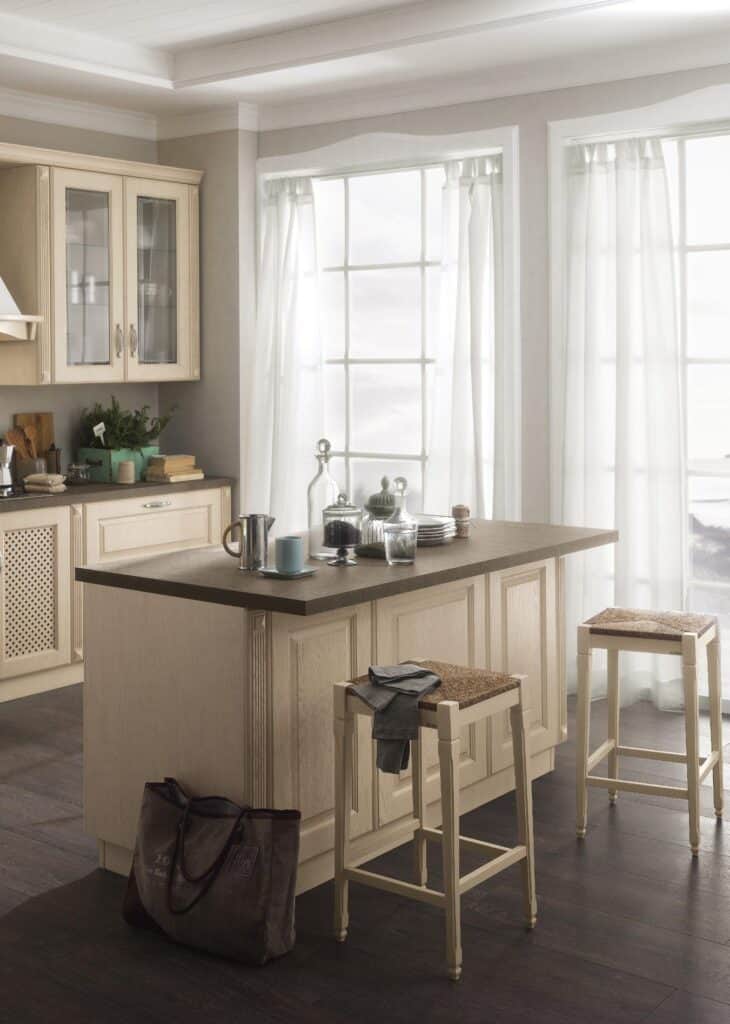 Cozy kitchen with beige cabinets, large windows with sheer curtains, and a central island with dark countertop and rustic stools.