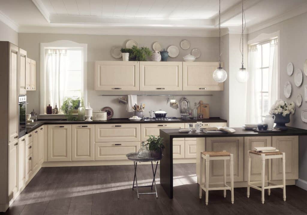 A cozy kitchen with cream-colored cabinets, dark countertops, pendant lighting, and a small breakfast bar with stools.