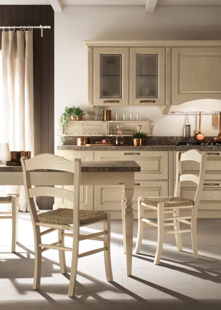 Cozy kitchen with wooden furniture, light-colored cabinets, table with wicker chairs, and decorative plants on the counter.