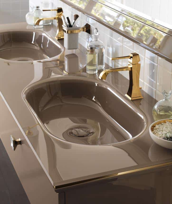 Double bathroom sink with a sleek brown surface and gold faucets, accompanied by toiletries and a bowl of decorative stones.