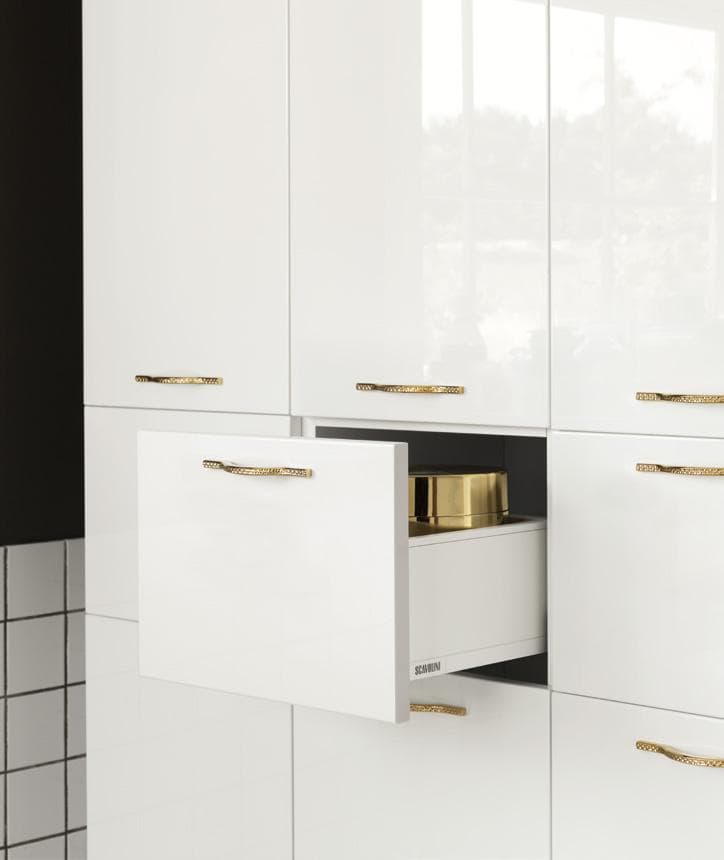 White glossy cabinet with gold handles, one drawer partially open revealing a gold-lidded container.