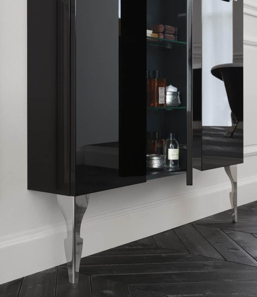 Sleek black cabinet with glass door, displaying toiletries and silver storage containers, against a white wall and dark herringbone floor.