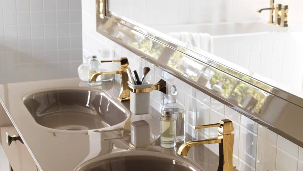 Elegant bathroom vanity with dual sinks, gold faucets, a large mirror, and various toiletry items on the counter.