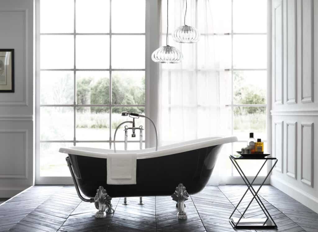 Freestanding black bathtub with clawfoot design in a bright bathroom with large window and a side table holding toiletries.