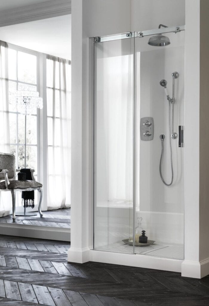Modern bathroom with a glass shower enclosure, featuring a rain showerhead and handheld shower, adjacent to a room with wooden herringbone flooring and armchair.