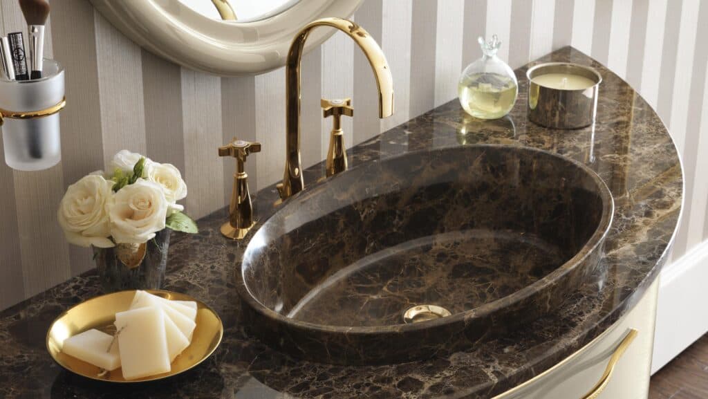 Luxurious bathroom sink with dark marble countertop, gold faucet, and elegant decor including white roses, a candle, and soap on a gold plate.