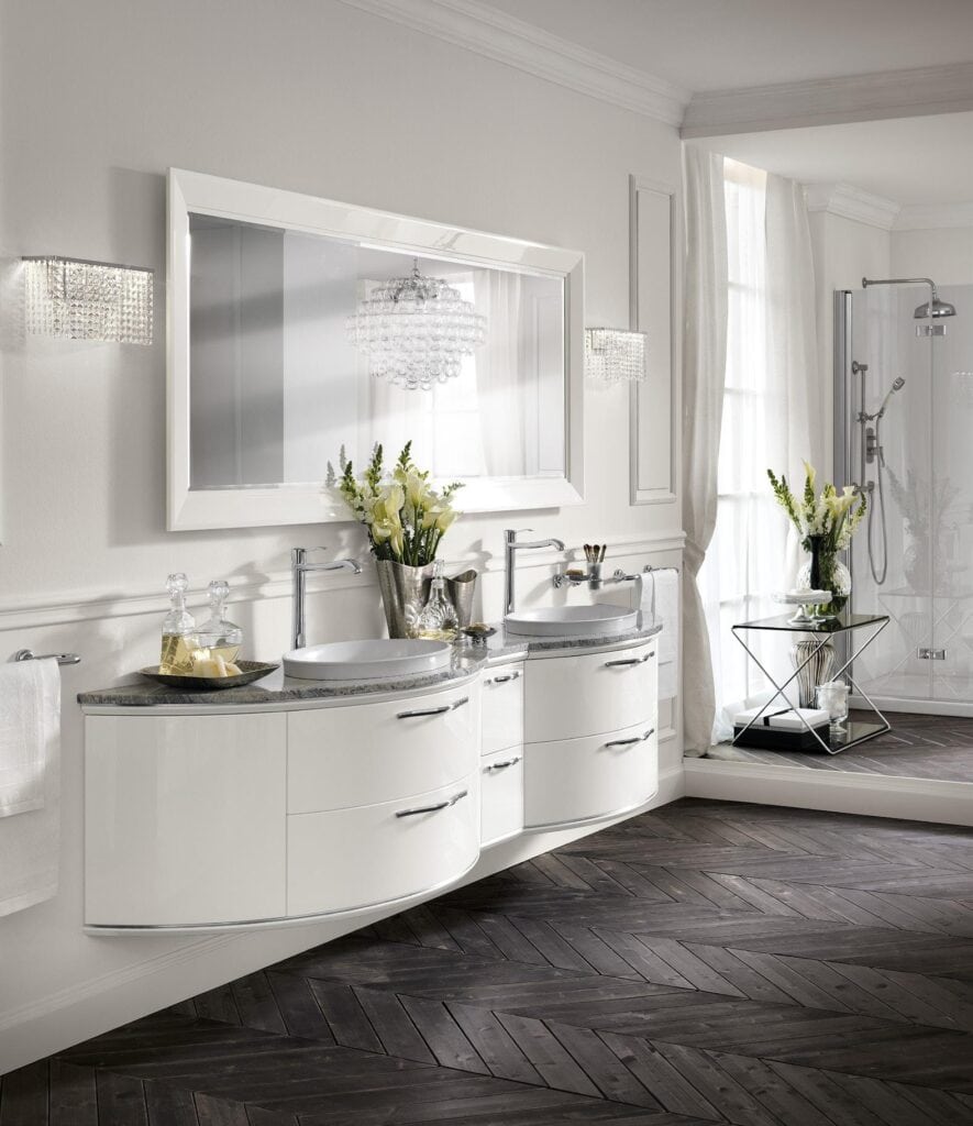 Luxurious bathroom with double sink vanity, large mirror, elegant lighting fixtures, and herringbone patterned dark wood floor.